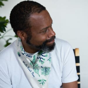 Smiling man with a beard wearing a white shirt and patterned scarf.