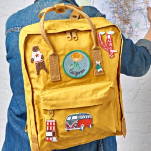 Yellow backpack with colorful patches and pins, worn by a child.