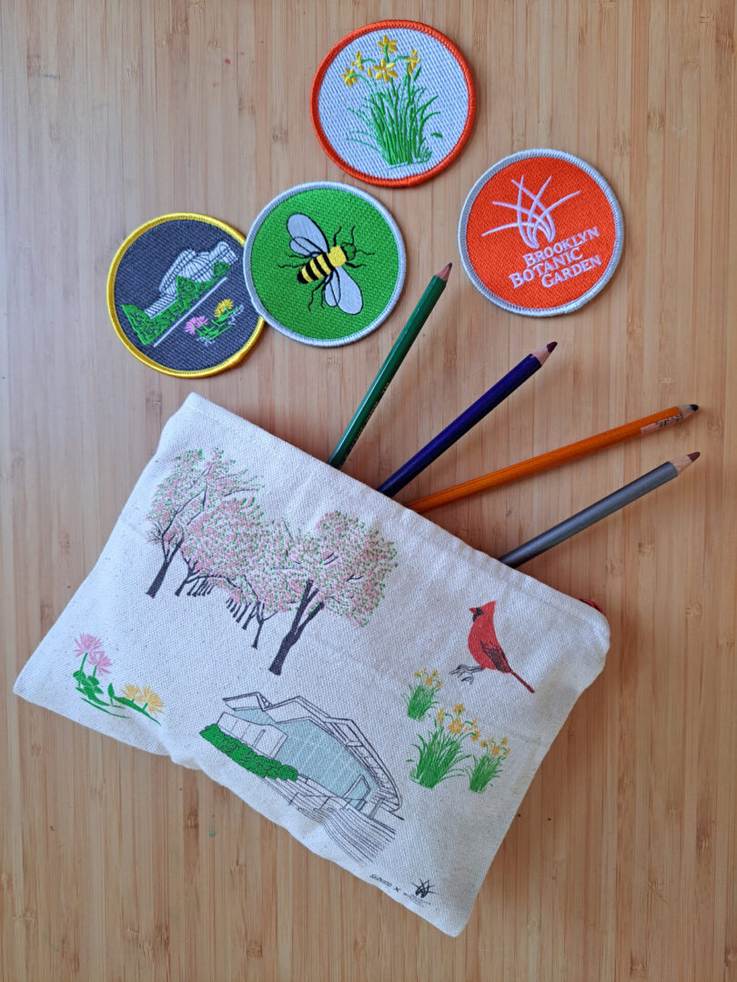Decorative pencil case with nature-themed embroidery and colorful pencils on a wooden surface.