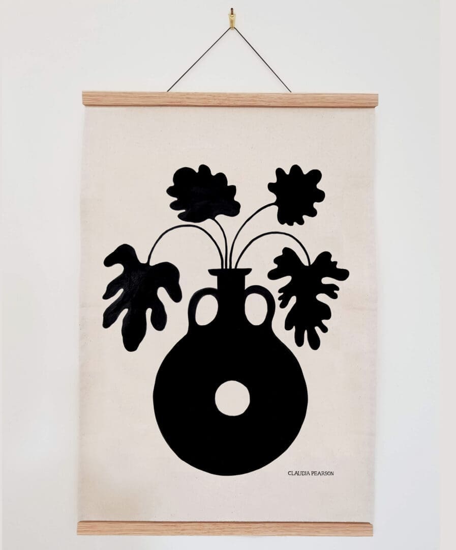 Minimalist wall art with black silhouette of a vase and leaves on beige fabric.