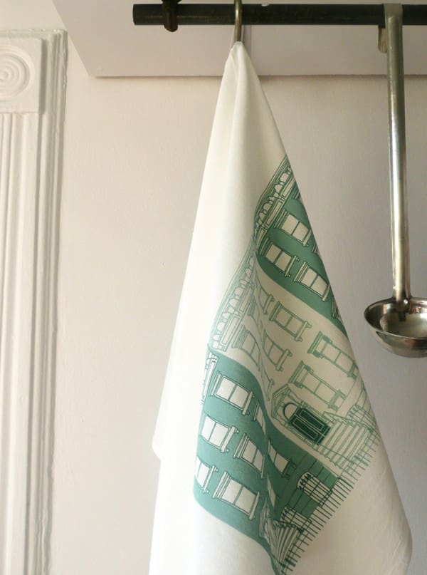White kitchen towel with green printed designs hanging on a hook.