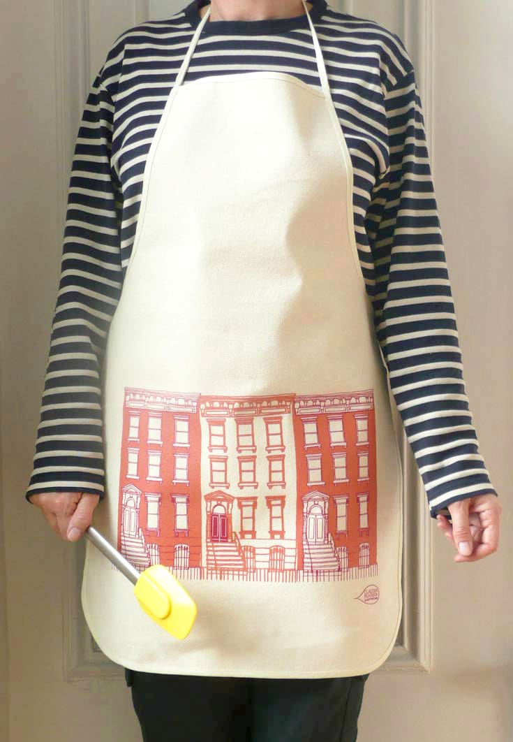 Child wearing a striped shirt and apron with a building print, holding a yellow spatula.