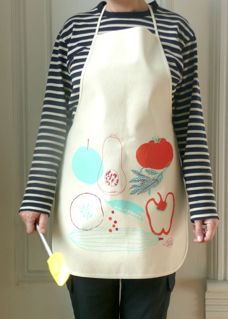 Person wearing a white apron with colorful vegetable prints over a striped shirt.